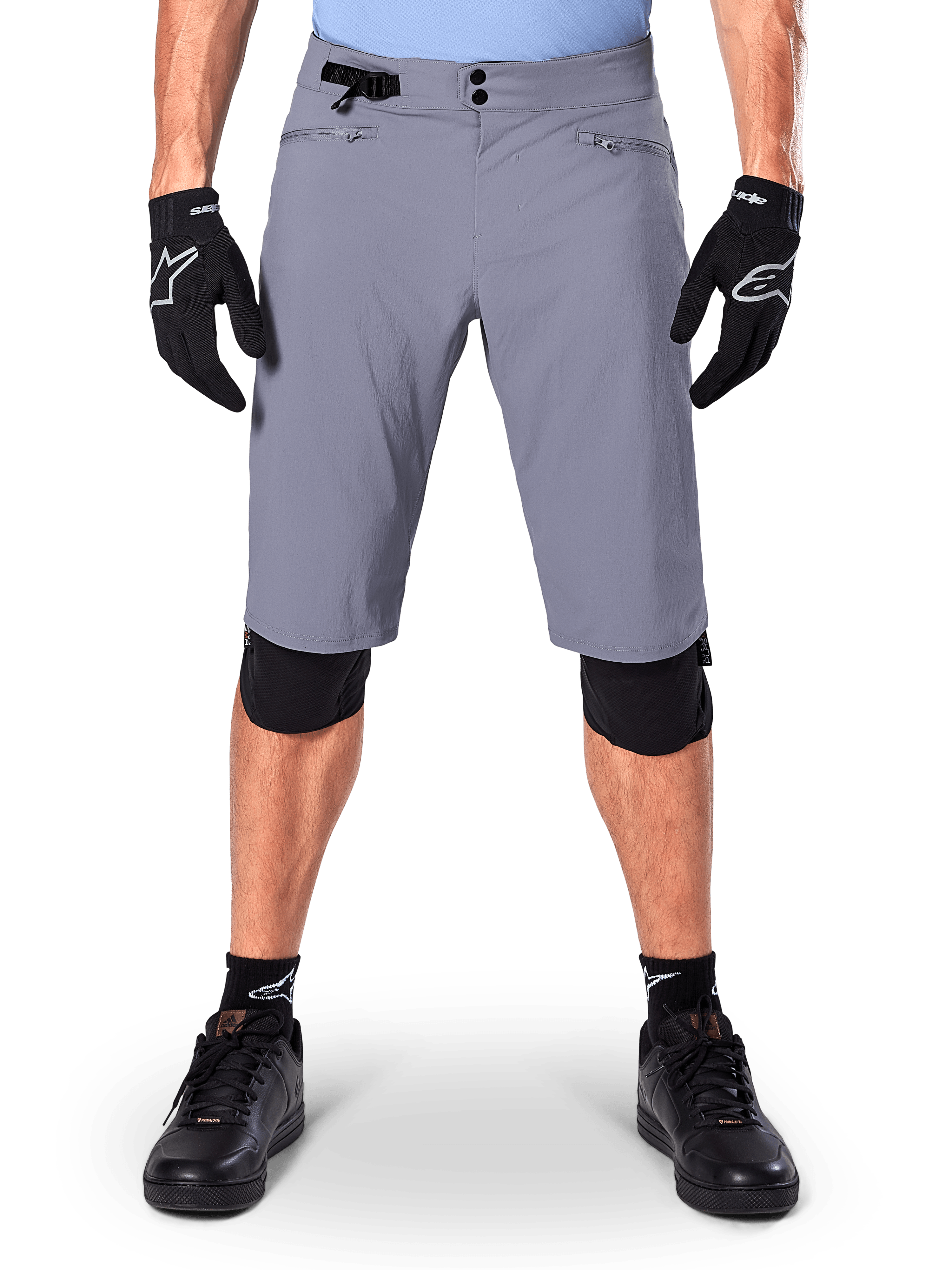 Short Alpinestars A-Dura, short de VTT, gris foncé, porté avec des gants et genouillères Alpinestars noirs, doté d'une double fermeture à pression et de poches zippées doublées en maille, tissu extensible 2 directions durable pour le cyclisme tout-terrain