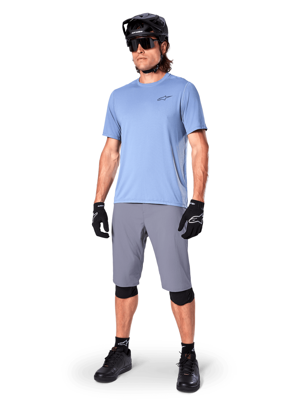 Short Alpinestars A-Dura, short de VTT, gris foncé, porté par un rider avec un maillot bleu clair, un casque de VTT noir, des gants noirs et des genouillères, tenue de VTT complète pour le trail et le tout-terrain
