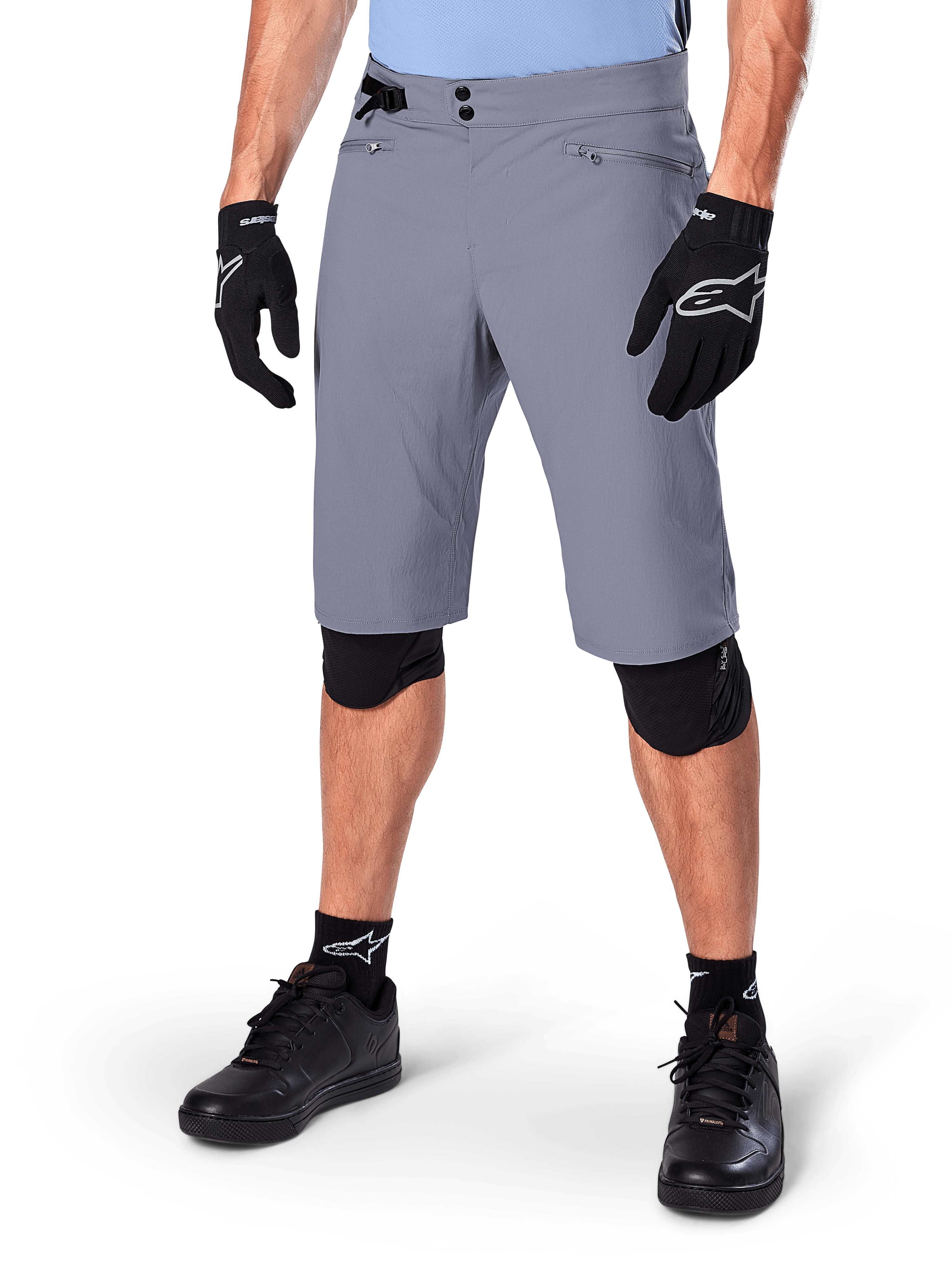Short Alpinestars A-Dura, short de VTT gris foncé, associé à des gants et des genouillères noirs, avec poches zippées et double fermeture à pression, équipement de cyclisme robuste pour les sentiers tout-terrain