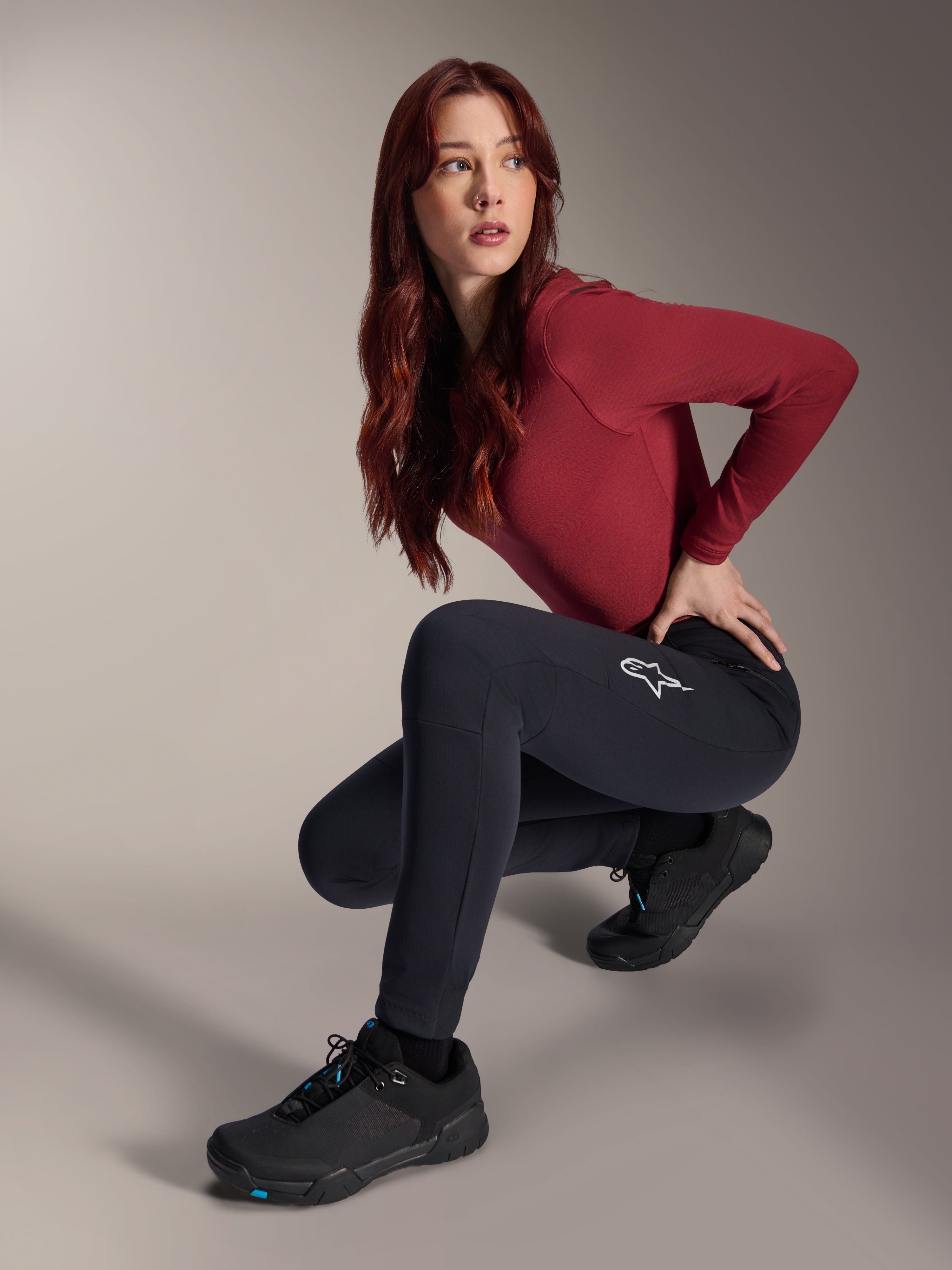 Pantalon thermique Alpinestars Stella A-Dura, pantalon de VTT pour femme, noir, porté par un mannequin accroupi avec un haut bordeaux à manches longues et des chaussures de cyclisme noires, logo étoile blanc sur la cuisse, construction chaude et durable pour les sorties tout-terrain par temps froid