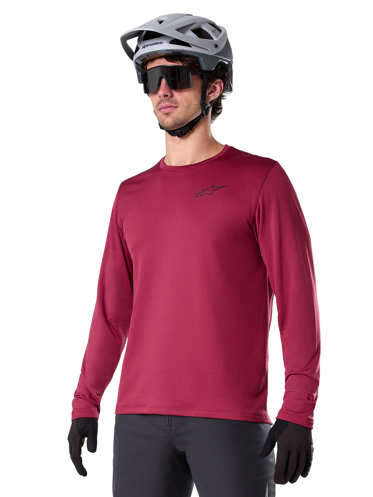 Maillot thermique Alpinestars A-Dura, maillot de VTT à manches longues, rouge bordeaux, avec doublure en polaire isolante et petit logo noir sur la poitrine, porté avec un casque gris, des lunettes de soleil noires et des gants noirs, conçu pour le cyclisme par temps froid
