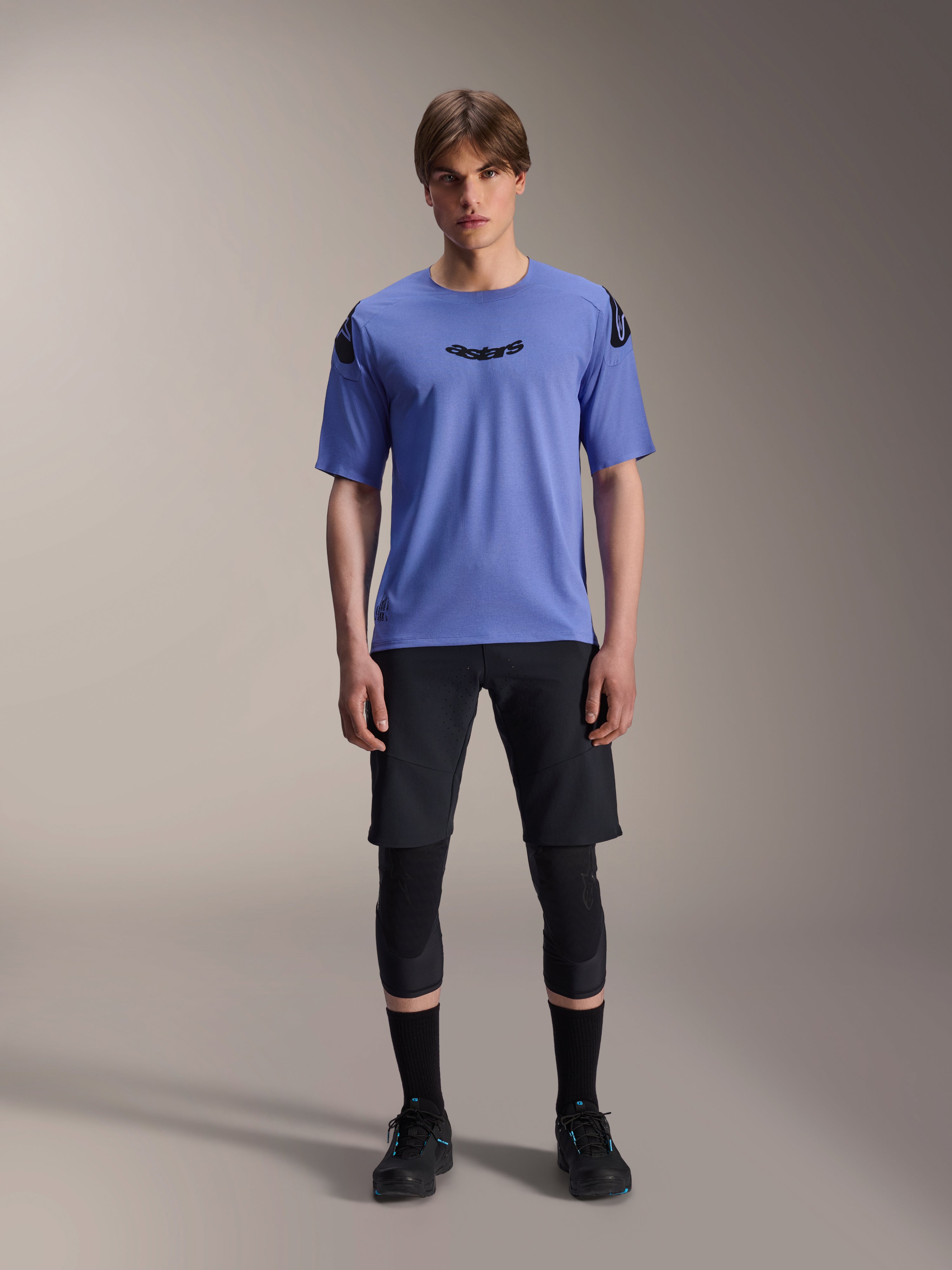 Alpinestars A-Aria Lite Short, short de VTT pour homme, noir, porté avec un maillot à manches courtes violet clair et des genouillères noires, vêtement de VTT performance