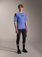 Mannequin portant un short Alpinestars A-Aria Lite noir, associé à un maillot à manches courtes bleu A-Aria Polartec Elite, des genouillères noires et des chaussures de cyclisme noires, tenue de VTT haute performance pour le trail.