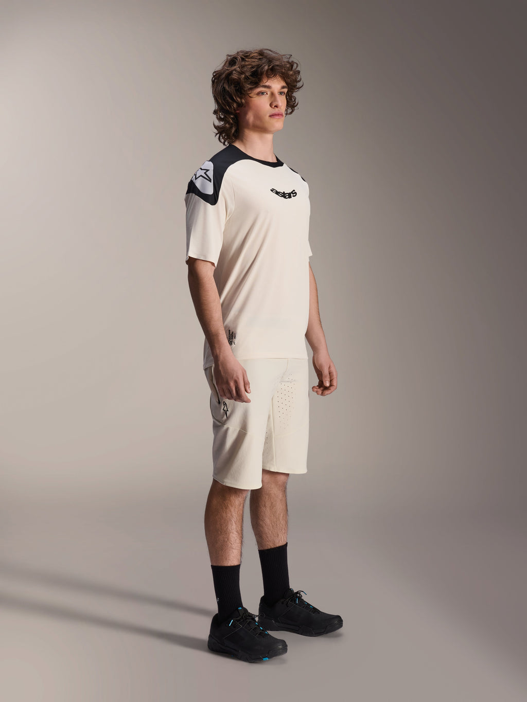 Maillot à manches courtes Alpinestars A-Aria Polartec Elite, écru avec empiècements noirs aux épaules et logo, porté par un mannequin avec un short assorti et des chaussures noires, vêtement de VTT haute performance pour la pratique sur sentiers.