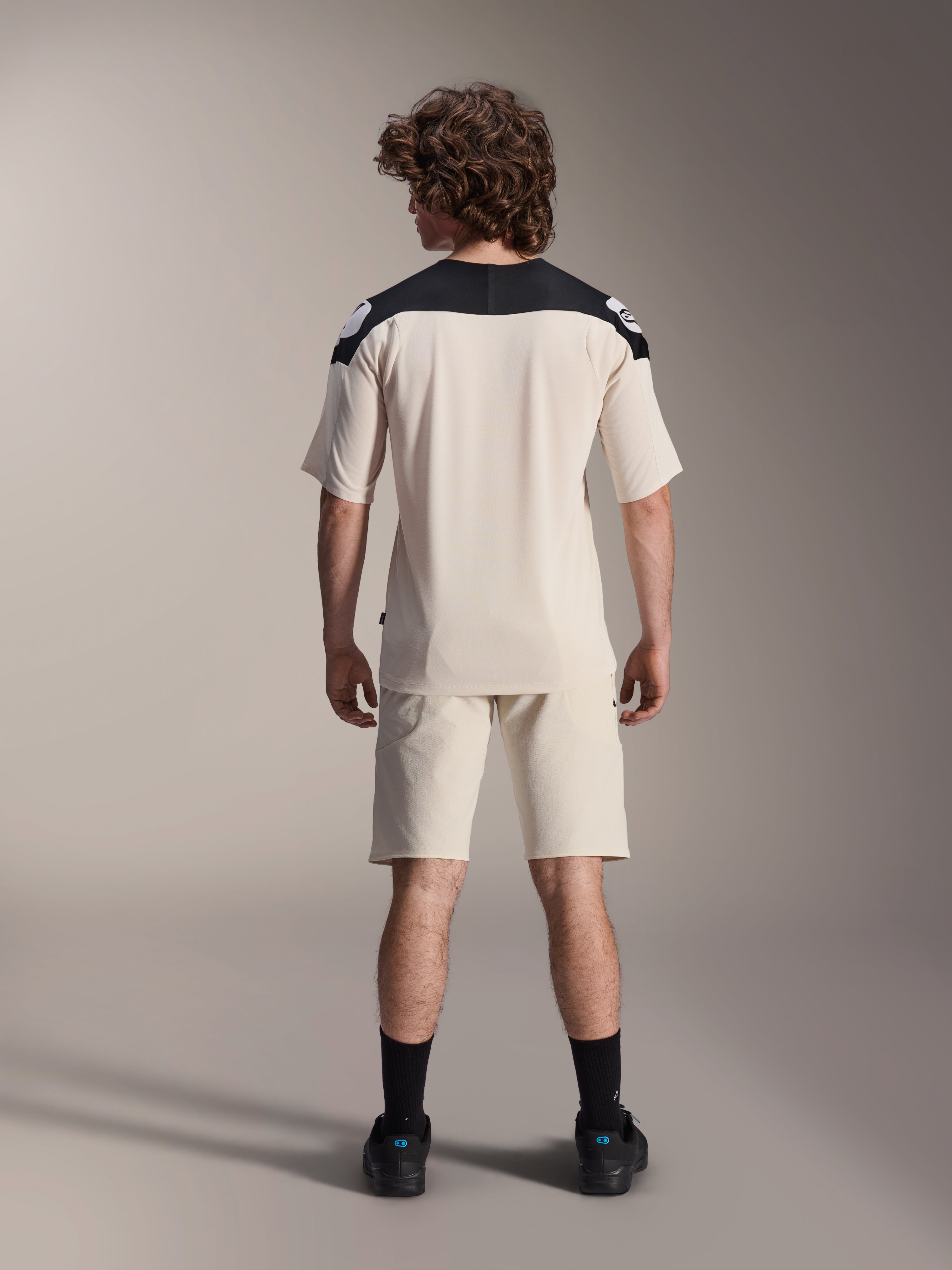 Maillot à manches courtes Alpinestars A-Aria Polartec Elite, maillot de cyclisme VTT, écru avec empiècements noirs aux épaules, vue de dos avec short assorti et chaussettes noires, coupe performance avec un design à queue tombante pour le tout-terrain.