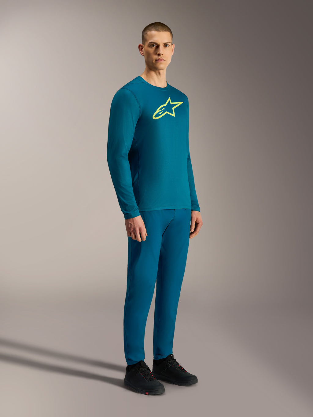 Maillot à manches longues A-Dura Ride bleu-vert avec logo Astars jaune, porté avec un équipement VTT assorti.