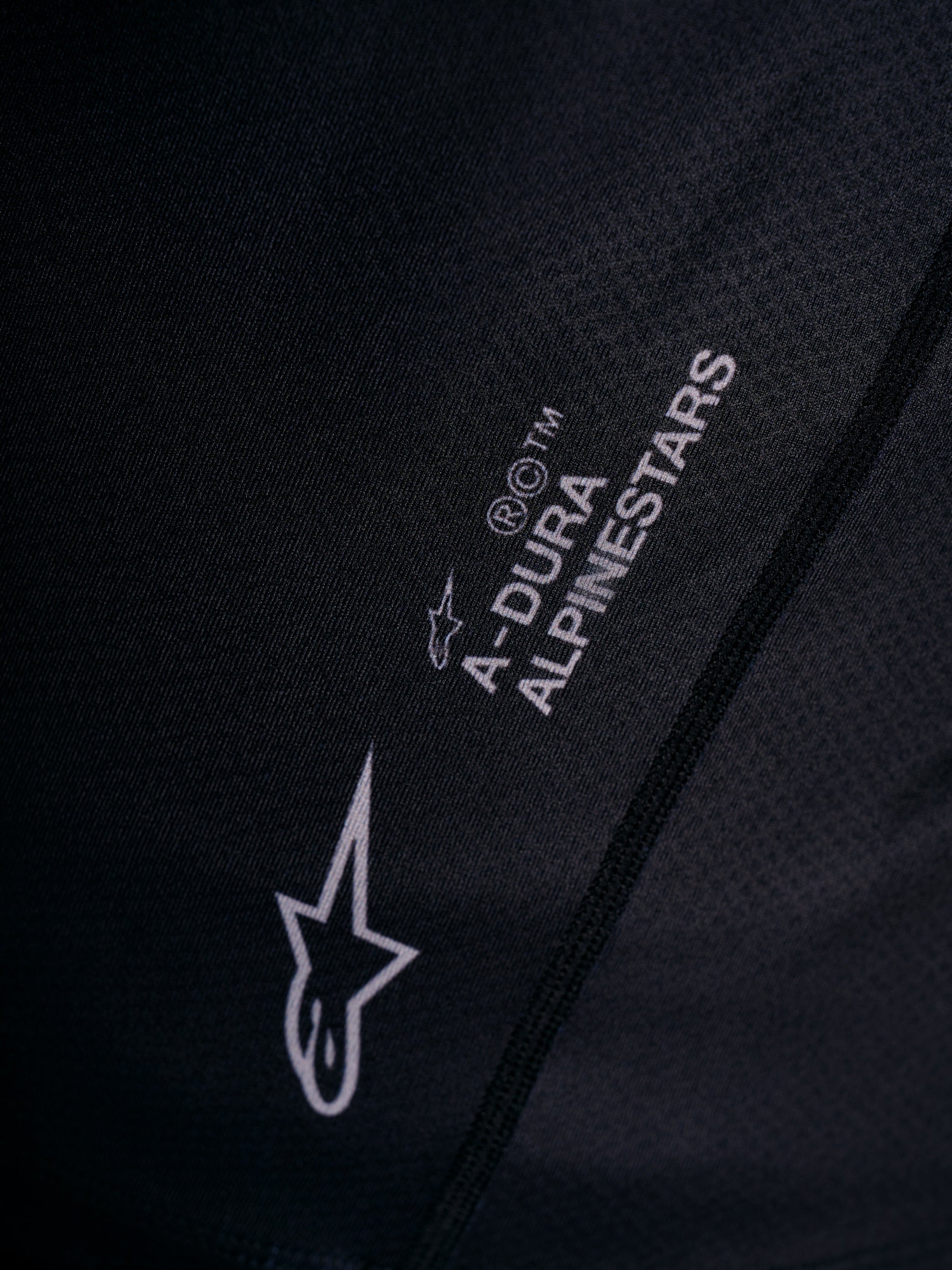 White Astars logo and A-DURA wordmark printed on the black A-Dura Ride Jersey, featuring technical jacquard mesh detail.
