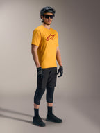 Maillot A-Dura Ride orange à manches courtes avec logo Astars rouge, associé à un équipement de VTT et un casque noirs.