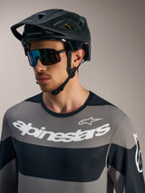 Maillot gris Alpinestars A-Dura Race à manches longues avec logos blancs, casque de VTT noir et lunettes de soleil.