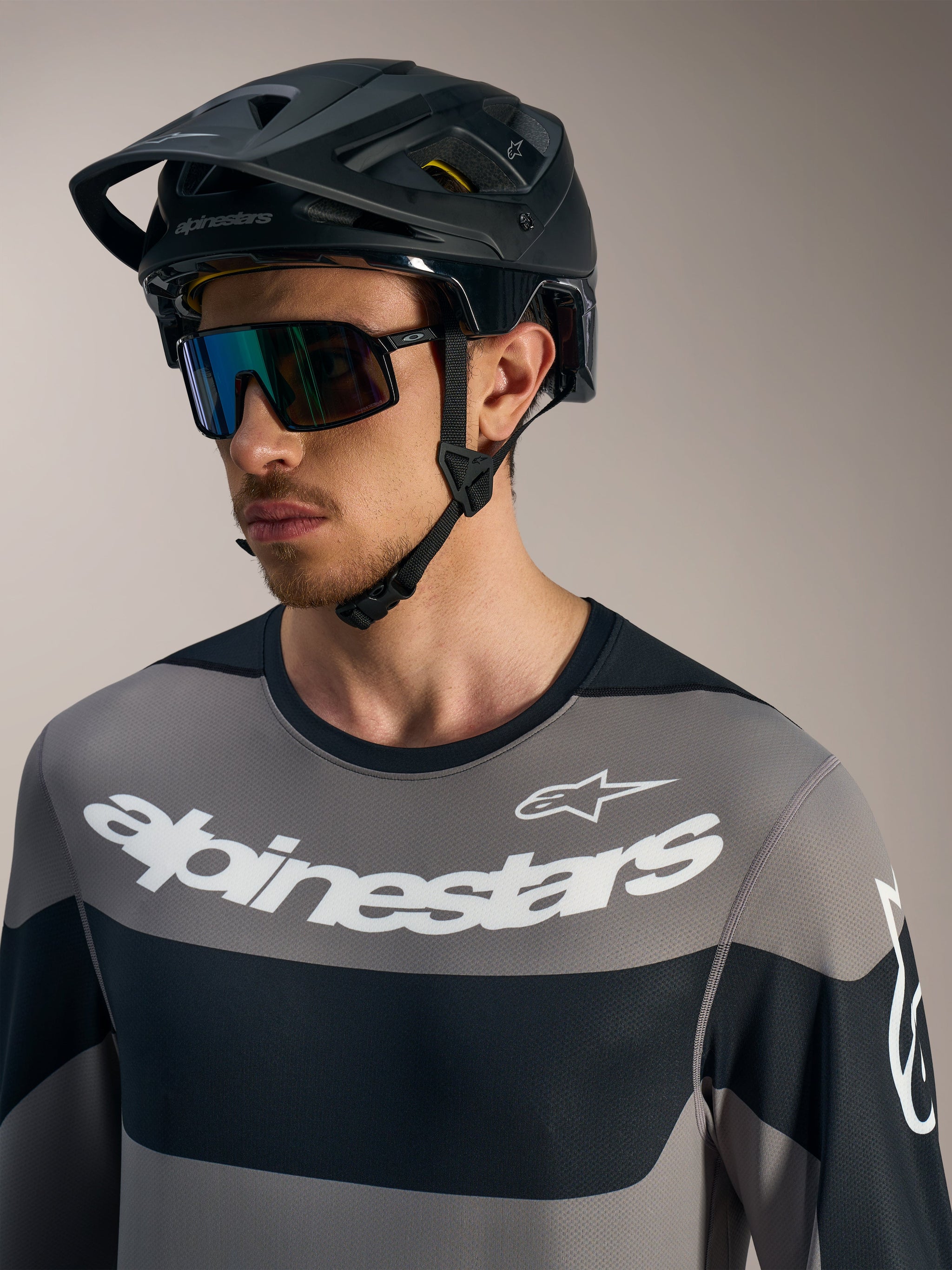 Maillot gris Alpinestars A-Dura Race à manches longues avec logos blancs, casque de VTT noir et lunettes de soleil.