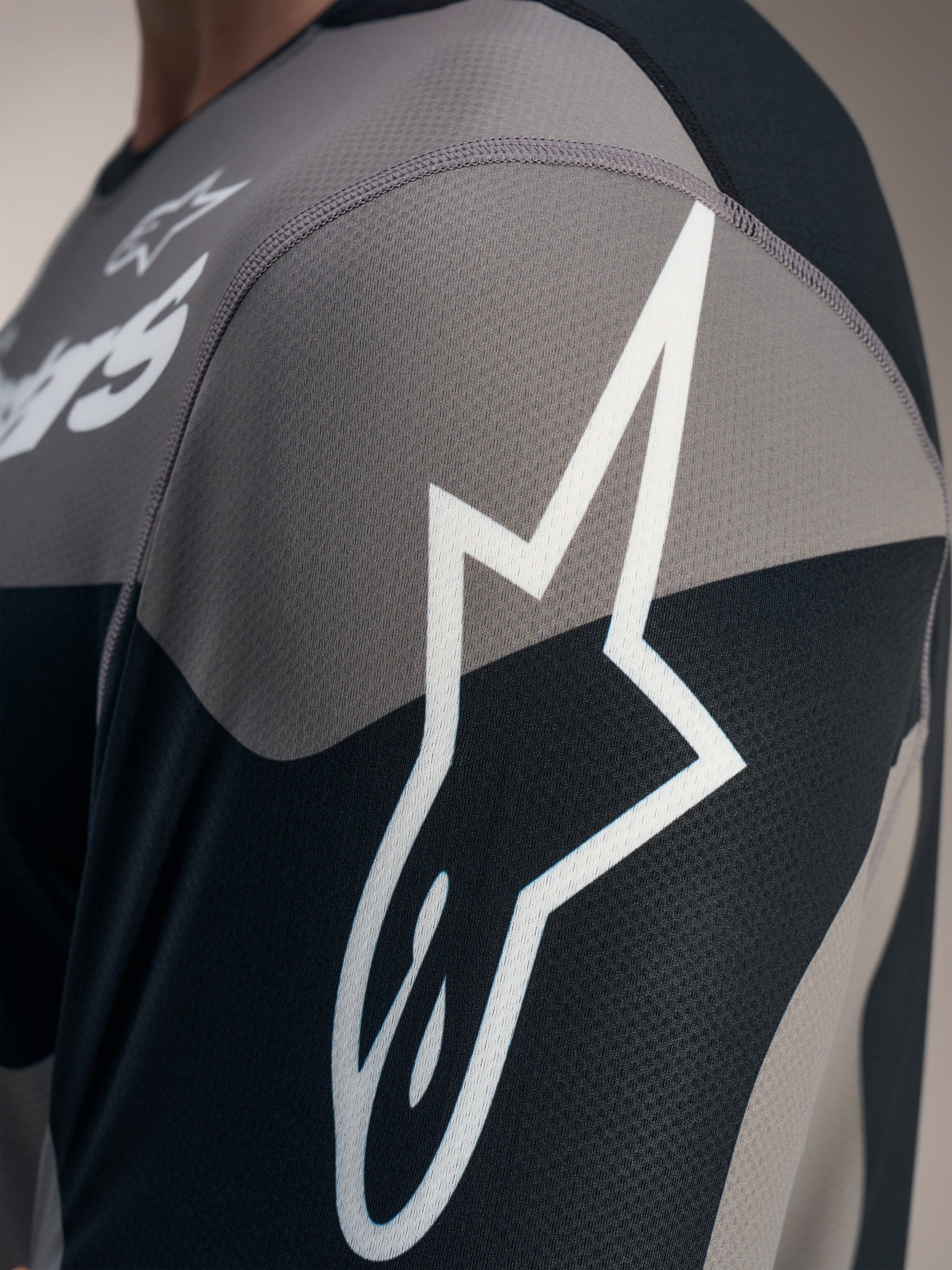 Maillot A-Dura Race gris, gros plan sur le logo Astars blanc et le tissu technique en maille jacquard.
