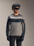 Maillot A-Dura Race manches longues gris et noir, logo blanc Alpinestars, porté avec un casque de VTT pour le trail.