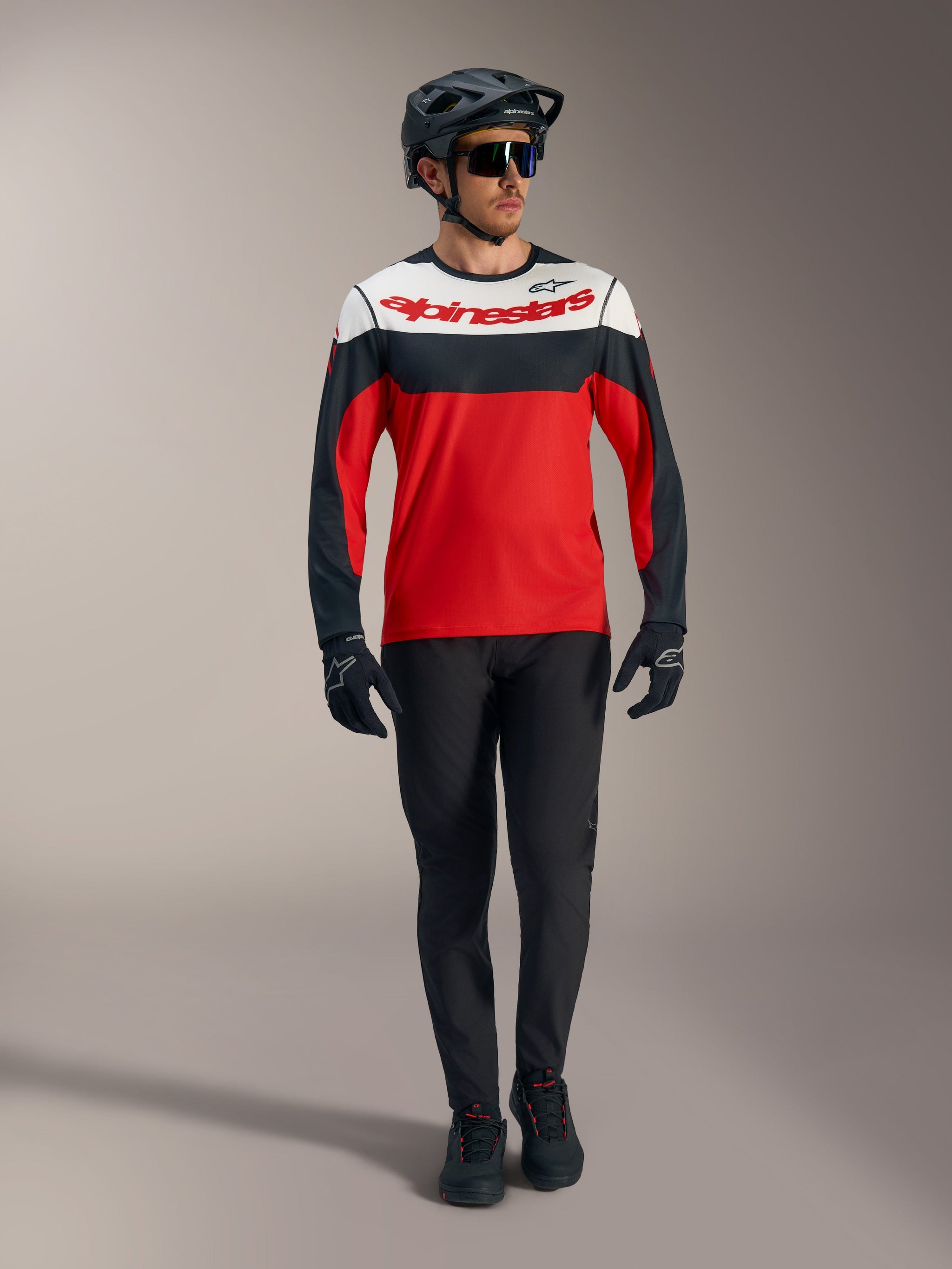 Maillot Alpinestars A-Dura Race rouge à manches longues, panneaux noirs et blancs, avec pantalon VTT et casque protecteur.