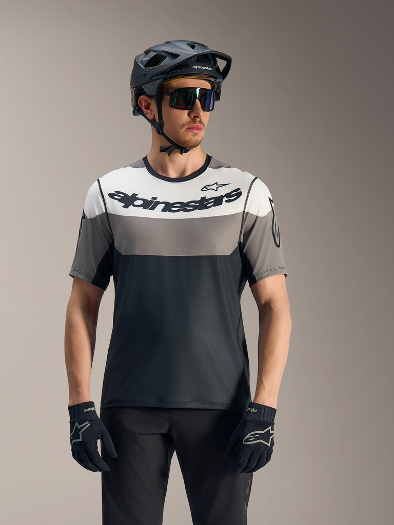 Maillot A-Dura Race à manches courtes gris et noir, logo Alpinestars, avec casque VTT et lunettes de protection.