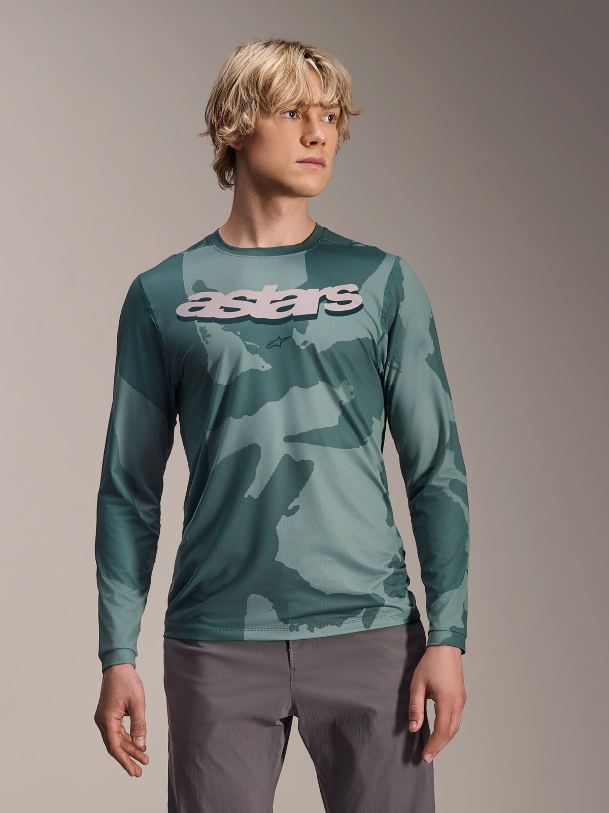 Maillot à manches longues Alpinestars A-Dura Hollow Camo, maillot de VTT, motif camouflage vert Silver Pine Camo, grand logo astars gris clair sur la poitrine, porté avec un pantalon gris, équipement de VTT haute performance