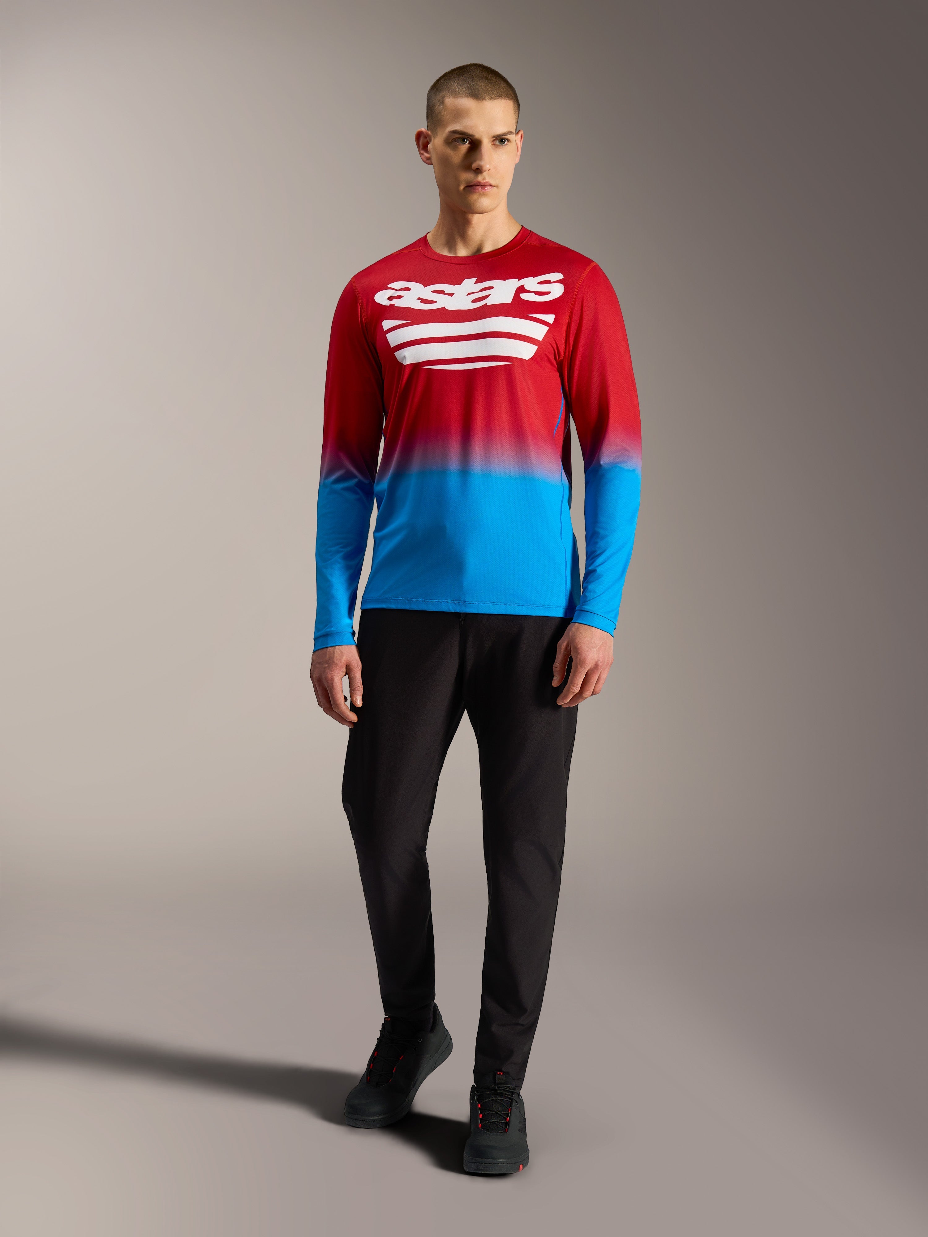 Maillot de VTT A-Dura ASTARS 2.0 à manches longues, dégradé rouge et bleu avec logos blancs, porté avec un pantalon noir.