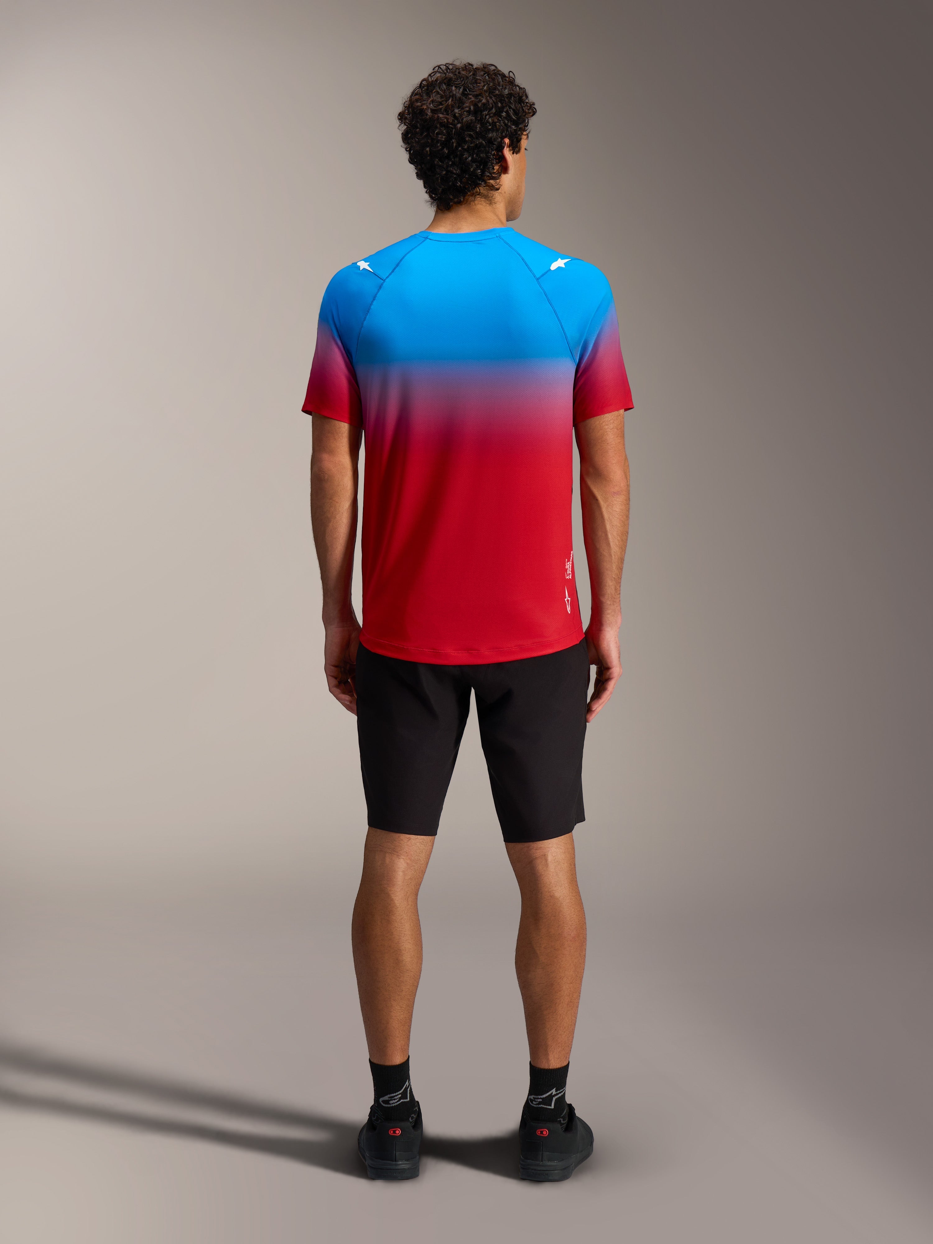 Maillot VTT A-Dura ASTARS 2.0, dégradé bleu et rouge, manches courtes, vu de dos avec short noir.