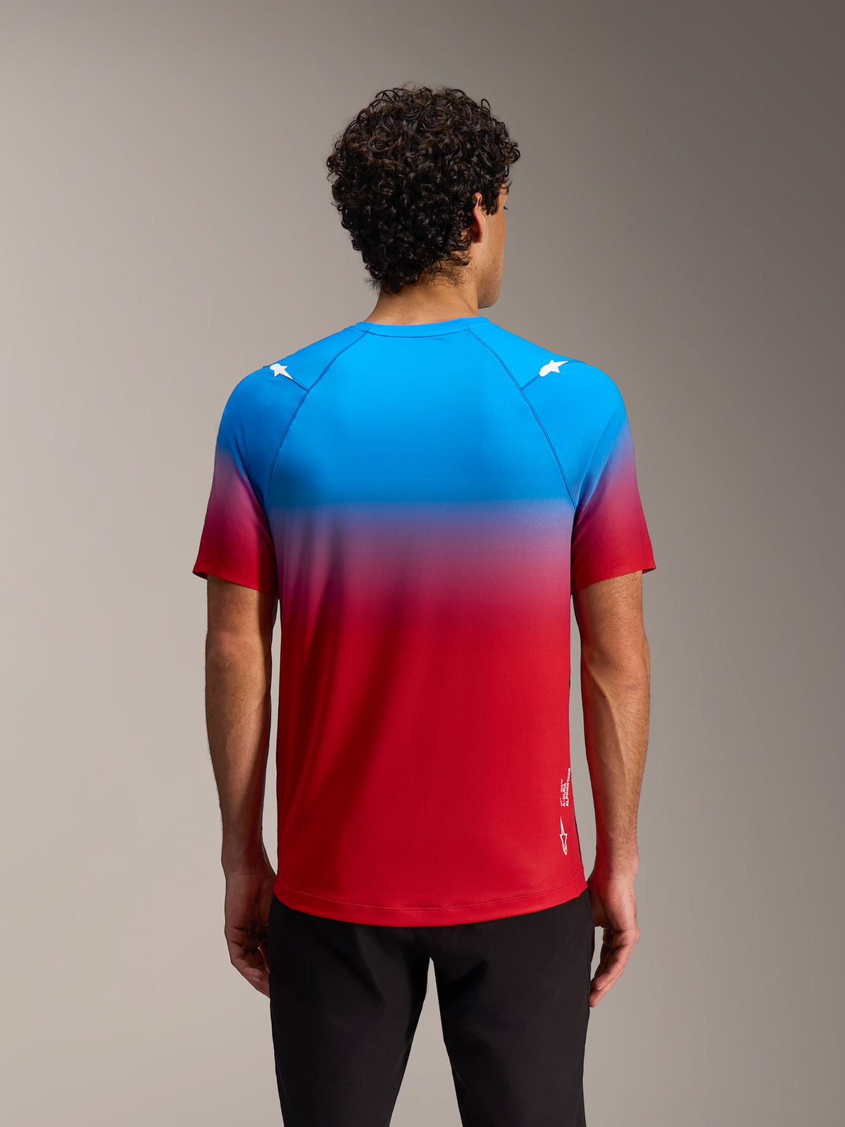 Maillot Alpinestars A-Dura ASTARS 2.0 dégradé bleu et rouge vif, logos étoile aux épaules, manches courtes, vue de dos.