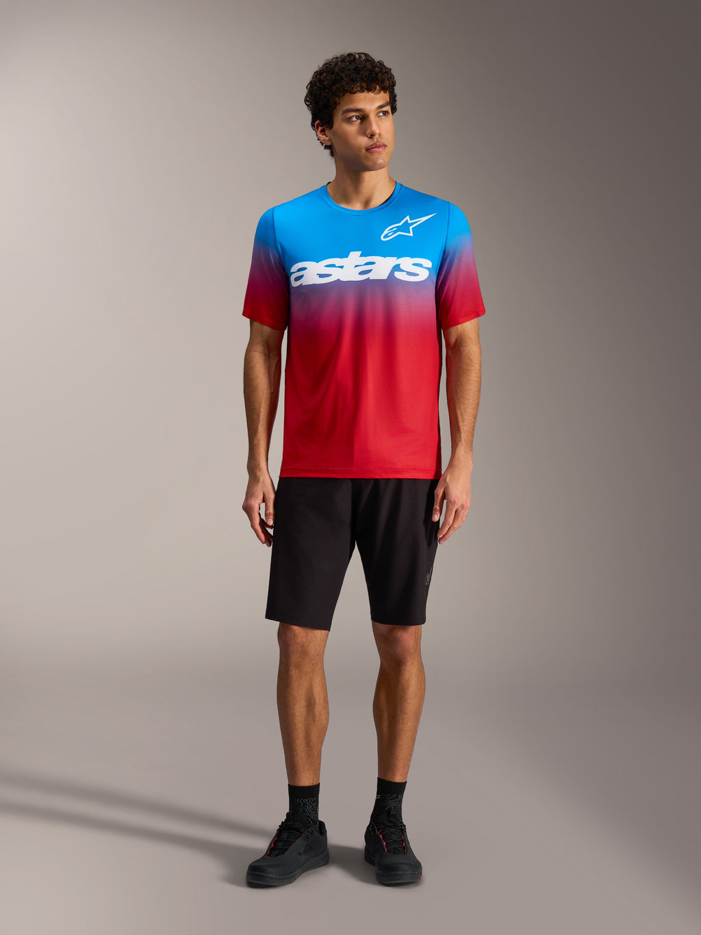 Maillot A-Dura ASTARS 2.0 dégradé rouge vif et bleu, logo blanc, avec short de VTT et chaussures noirs.