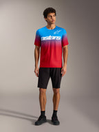 Maillot A-Dura ASTARS 2.0 dégradé rouge vif et bleu, logo blanc, avec short de VTT et chaussures noirs.
