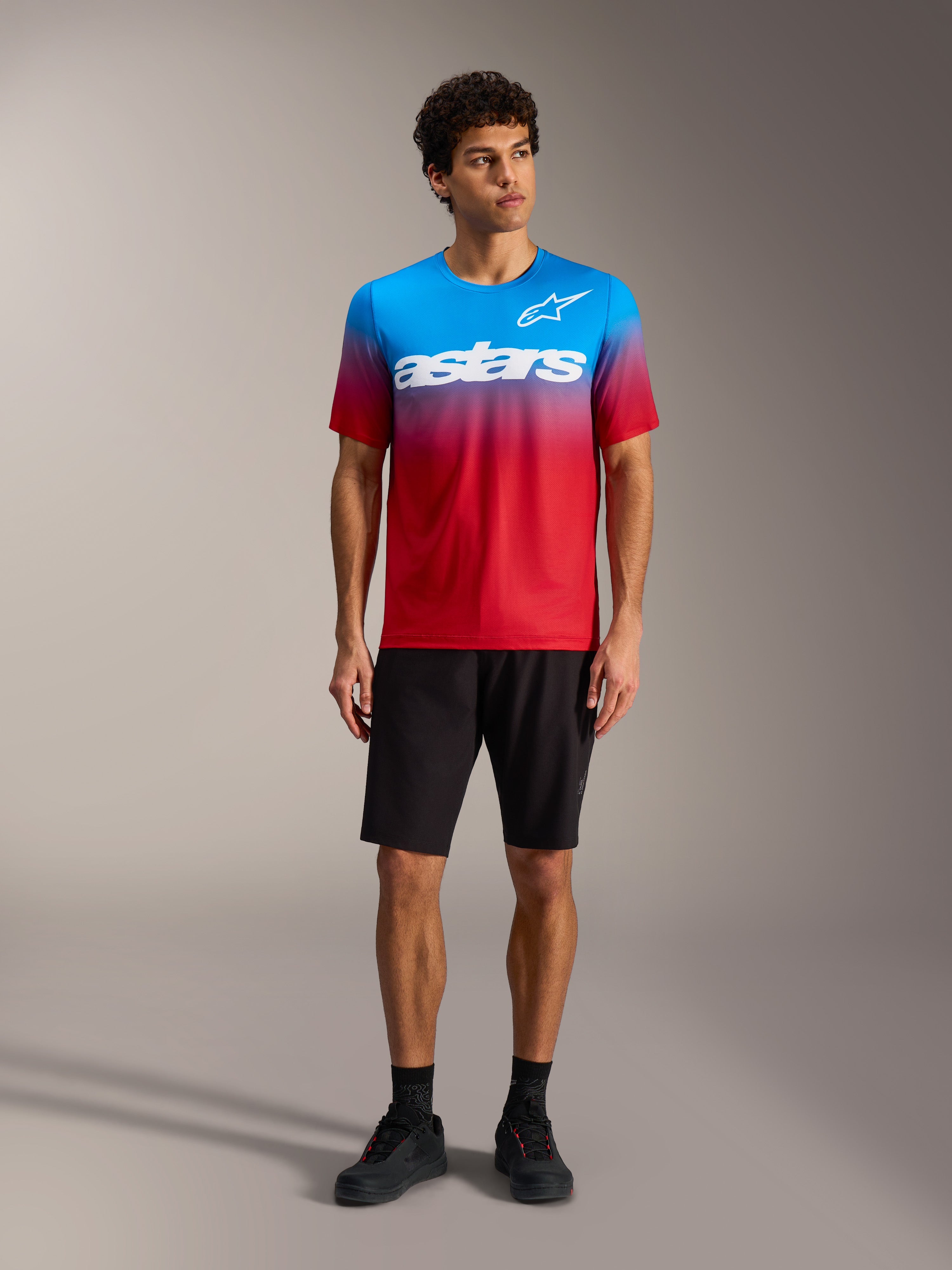 Maillot A-Dura ASTARS 2.0 dégradé rouge vif et bleu, logo blanc, avec short de VTT et chaussures noirs.
