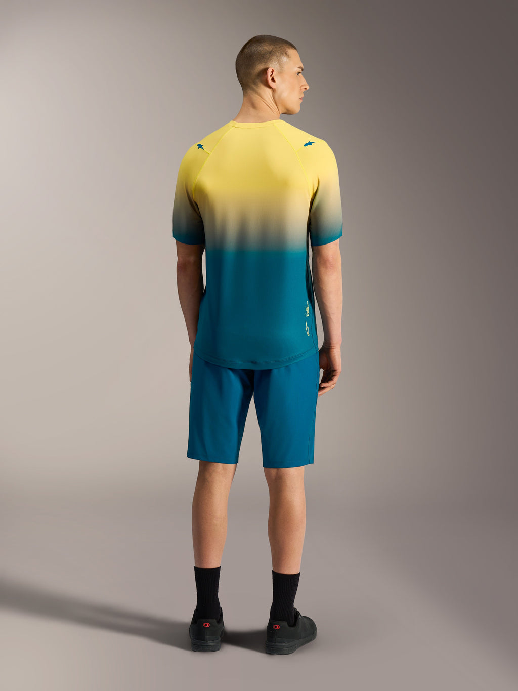Maillot VTT A-Dura ASTARS 2.0 à manches courtes, dégradé jaune et bleu-vert, présenté de dos sur un modèle.
