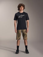 Maillot à manches courtes Alpinestars A-Dura Astar, noir avec un grand logo Astars blanc sur la poitrine, porté par un mannequin avec un short de VTT camouflage et des chaussures de cyclisme noires, vêtements de VTT décontractés.