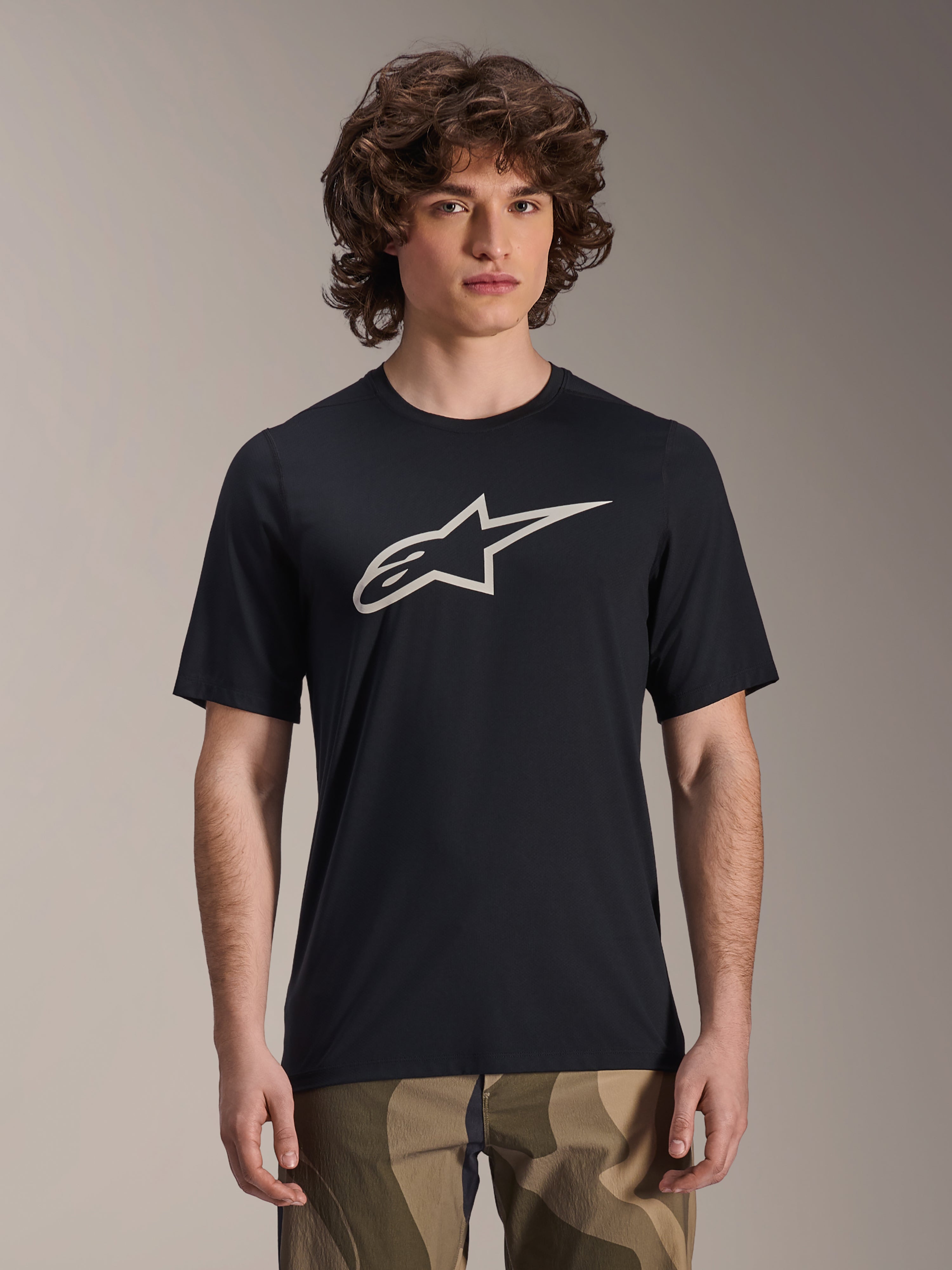 Maillot Alpinestars A-Dura Astar, maillot de VTT à manches courtes, noir avec logo étoile blanc, porté avec un pantalon camouflage, tenue de VTT décontractée, tissu technique évacuant l'humidité