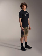 Maillot à manches courtes Alpinestars A-Dura Astar, noir avec logo blanc sur la poitrine, porté avec un short camouflage et des chaussures de VTT noires, équipement de VTT décontracté