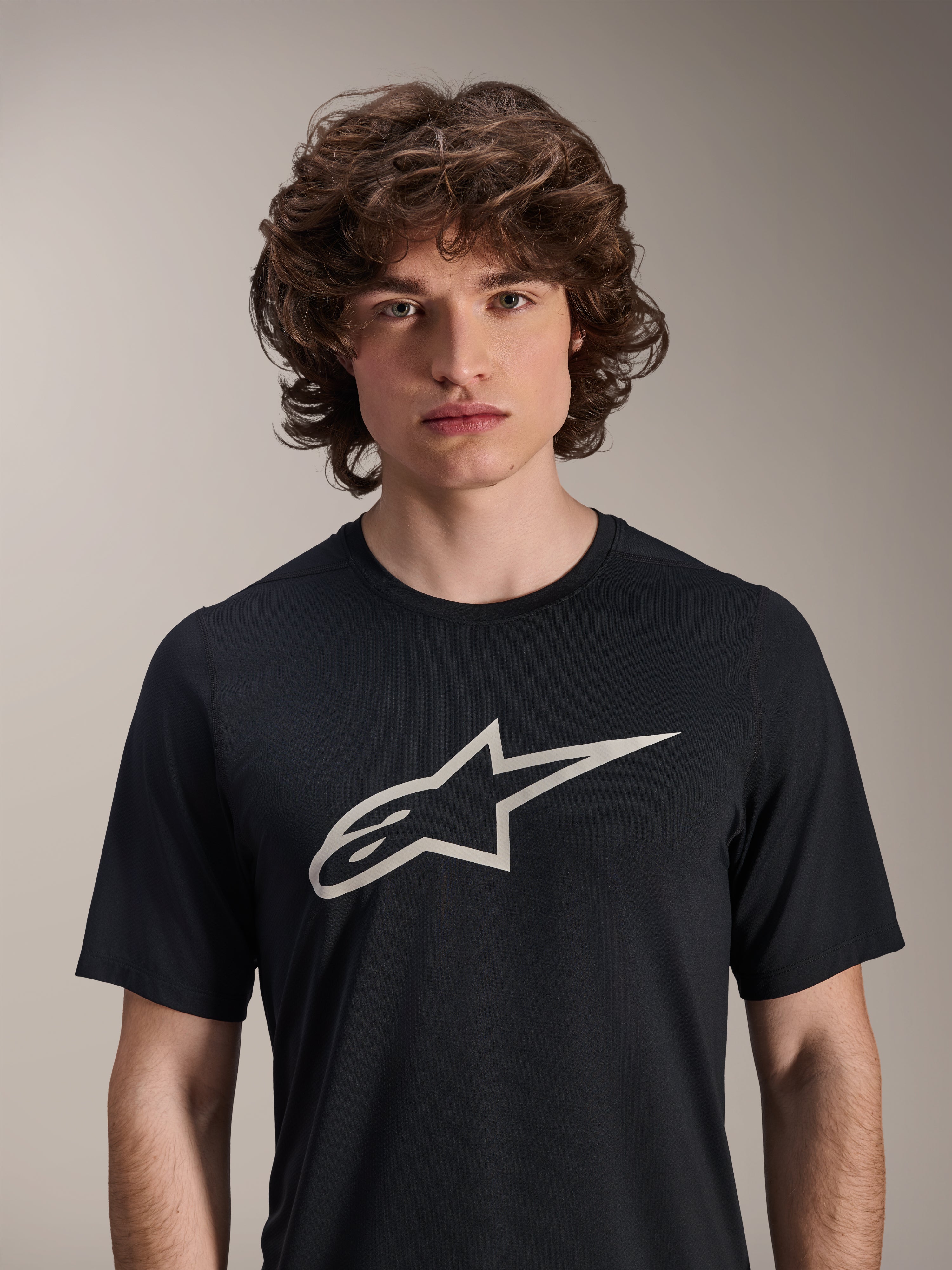 Maillot à manches courtes Alpinestars A-Dura Astar, noir, doté d'un grand logo Astar blanc sur la poitrine, porté par un mannequin homme, vêtement de performance décontracté pour le VTT
