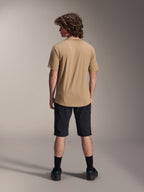 Modèle masculin vu de dos portant un short liner Alpinestars A-Dura noir et un maillot à manches courtes beige, avec des chaussettes et chaussures noires, équipement de VTT durable pour le cyclisme tout-terrain.
