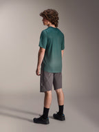 Maillot Alpinestars A-Dura Rise, maillot de VTT à manches courtes, vert Silver Pine, porté avec un short gris et des chaussures noires, vue arrière montrant la queue de pie plus longue et la coupe régulière, tissu léger évacuant l'humidité pour le VTT