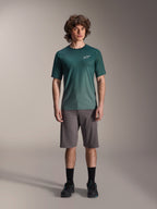 Modèle masculin portant le maillot Alpinestars A-Dura Rise à manches courtes en Silver Pine, maillot de cyclisme vert avec un petit logo blanc sur la poitrine, associé à un short de VTT gris et des chaussures noires, tenue de trail VTT décontractée
