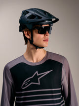 Maillot gris A-Dura Elite 2.0 à manches longues, logo noir, avec casque VTT et lunettes de soleil de performance.