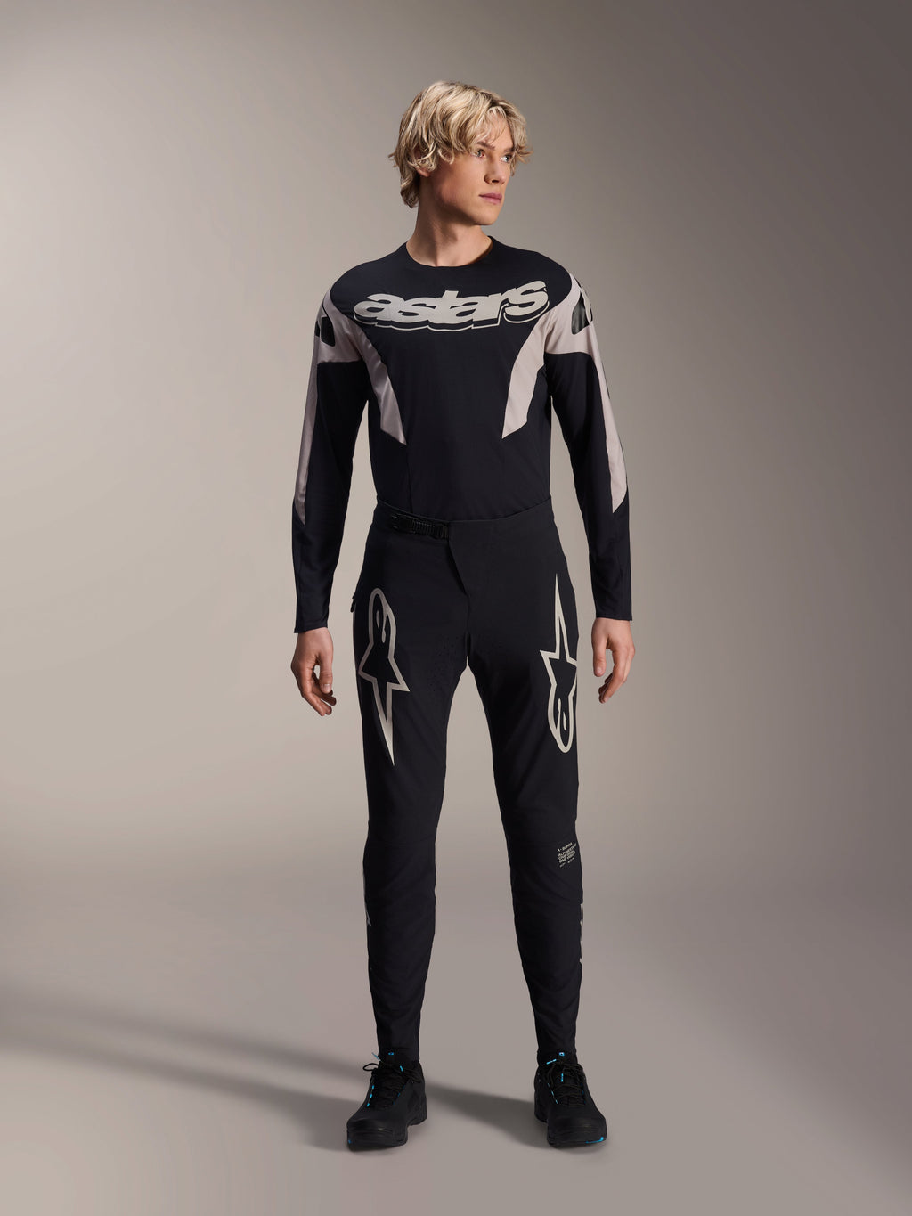 Pantalon Alpinestars A-Supra Melt et maillot à manches longues assorti, mannequin portant une tenue de VTT noire avec de grands graphismes d'étoiles blanches sur les cuisses et marquage 'astars' sur la poitrine, équipement de VTT professionnel