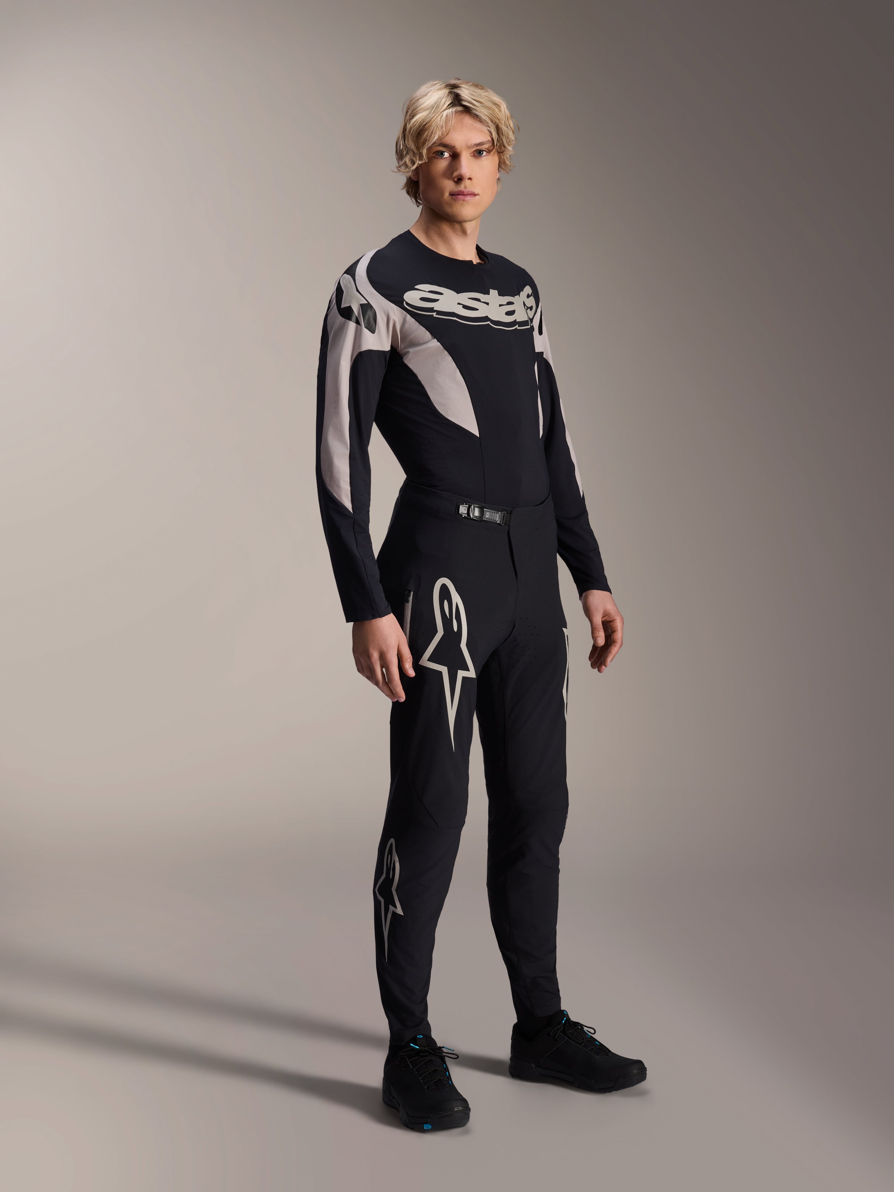 Mannequin homme portant le pantalon Alpinestars A-Supra Melt et le maillot à manches longues assorti, noir avec motifs incurvés gris clair, avec logos Astars blancs sur les jambes et logo textuel sur la poitrine, tenue de course de VTT professionnelle.