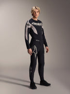 Modèle masculin portant le maillot Alpinestars A-Supra Melt à manches longues, noir avec des accents graphiques gris, logo 'astars' sur la poitrine, associé à un pantalon et des chaussures noirs assortis, équipement de VTT haute performance pour la course tout-terrain