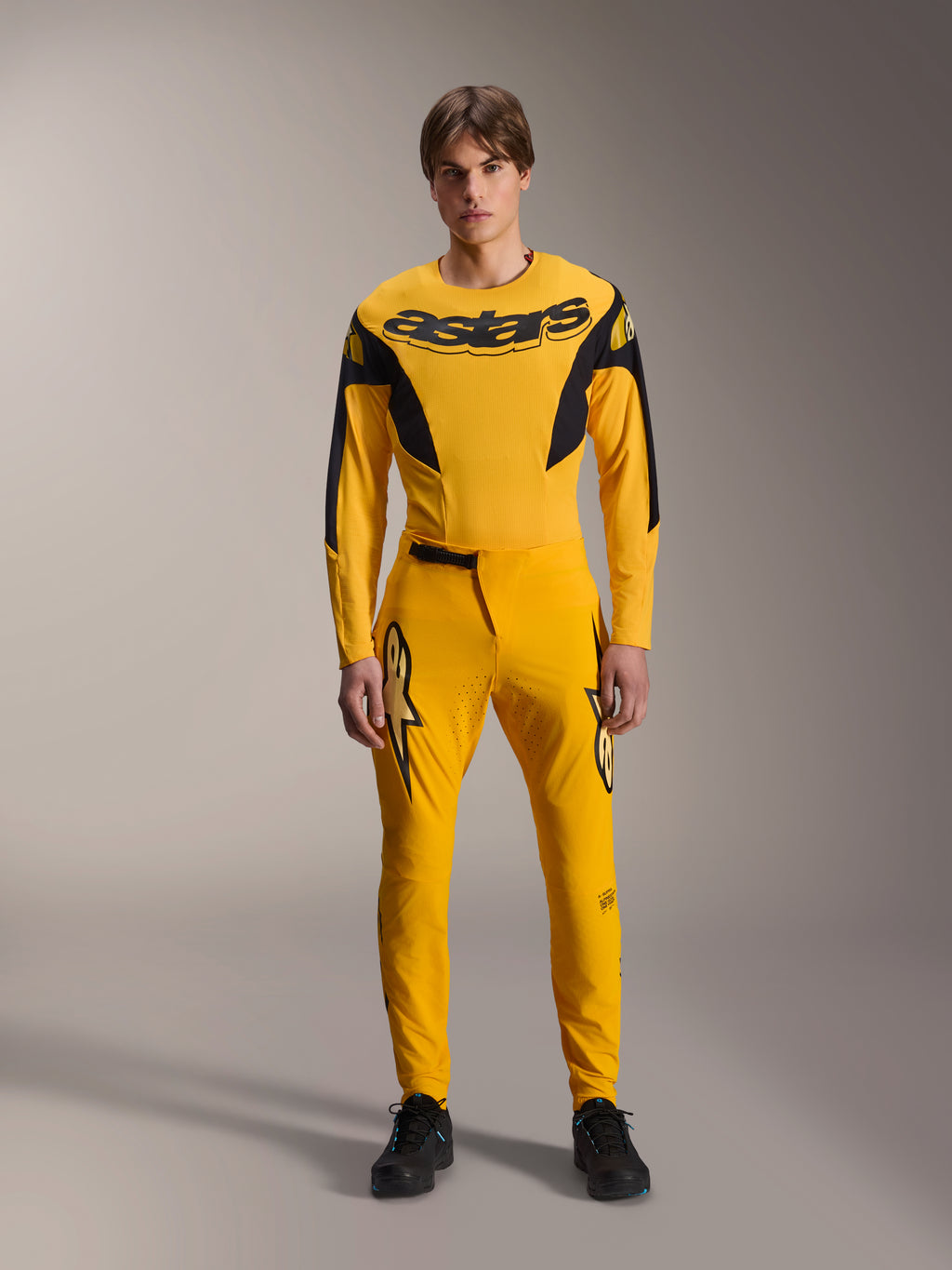 Ensemble d'équipement Limited Edition A-Supra Melt Gold, vêtements de VTT Alpinestars, jaune foncé et noir, modèle portant un maillot à manches longues avec logo 'astars' audacieux sur la poitrine et un pantalon de performance assorti, doté de ventilations découpées au laser sur l'intérieur des cuisses et d'une fermeture à cliquet sécurisée à la taille, tenue de course VTT professionnelle
