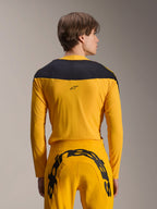 Set d'Équipement Limited Edition A-Supra Melt Gold Alpinestars, tenue de VTT jaune, vue arrière d'un mannequin portant un maillot à manches longues avec empiècement noir aux épaules et un pantalon jaune assorti arborant un grand logo noir à l'arrière, vêtements de cyclisme haute performance.
