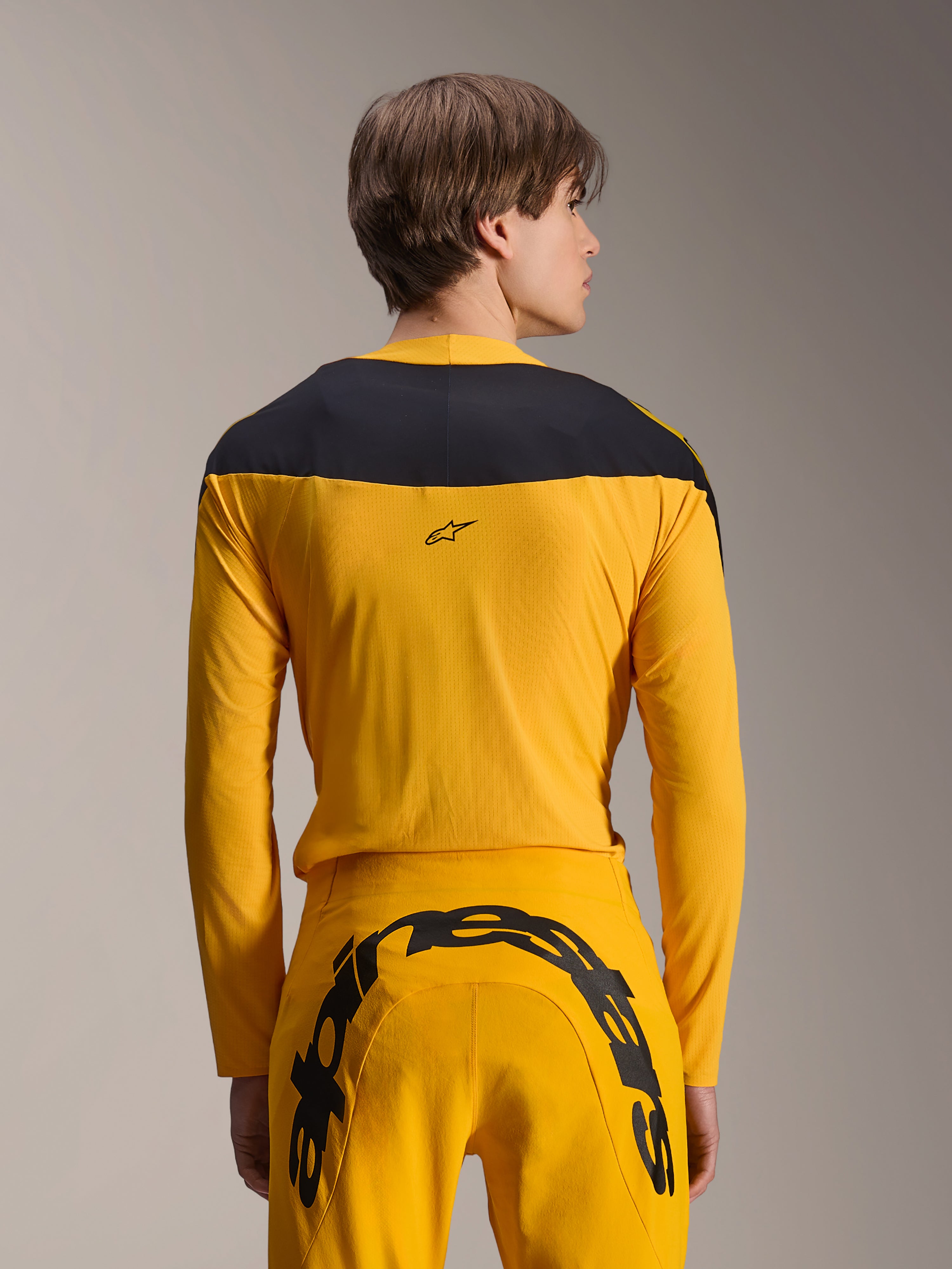 Set d'Équipement Limited Edition A-Supra Melt Gold Alpinestars, tenue de VTT jaune, vue arrière d'un mannequin portant un maillot à manches longues avec empiècement noir aux épaules et un pantalon jaune assorti arborant un grand logo noir à l'arrière, vêtements de cyclisme haute performance.