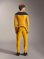 Vue arrière d'un mannequin portant l'ensemble d'équipement Alpinestars Limited Edition A-Supra Melt Gold, composé d'un maillot à manches longues jaune foncé avec un empiècement noir aux épaules et d'un pantalon jaune foncé assorti avec un grand marquage Alpinestars noir sur l'empiècement arrière, associé à des chaussures noires.