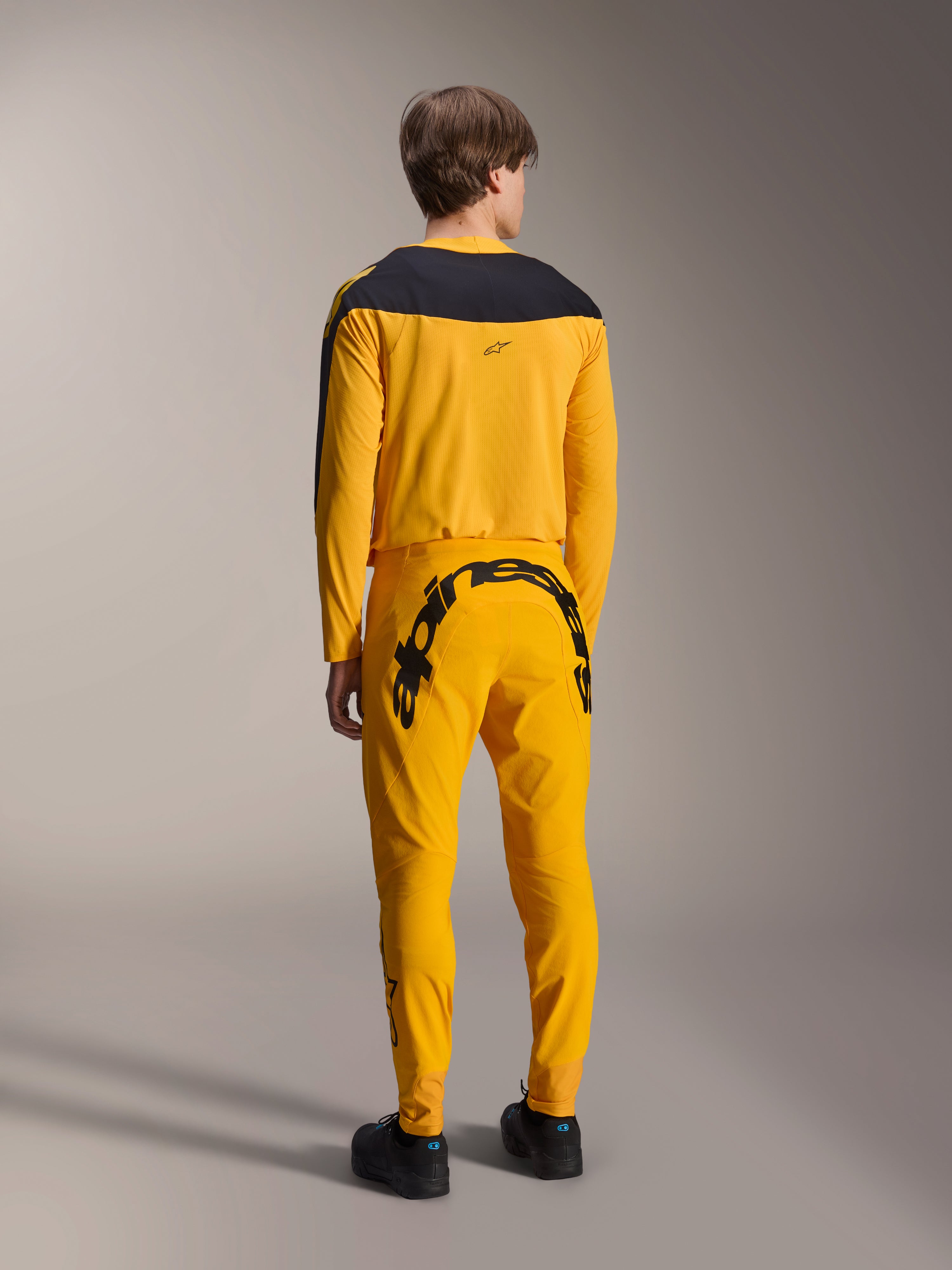 Maillot Alpinestars A-Supra Melt Gold Édition Limitée, maillot de VTT à manches longues, jaune foncé avec panneau noir aux épaules, porté avec un pantalon jaune assorti arborant un logo noir imposant à l'arrière, vue arrière d'une tenue de cyclisme de performance