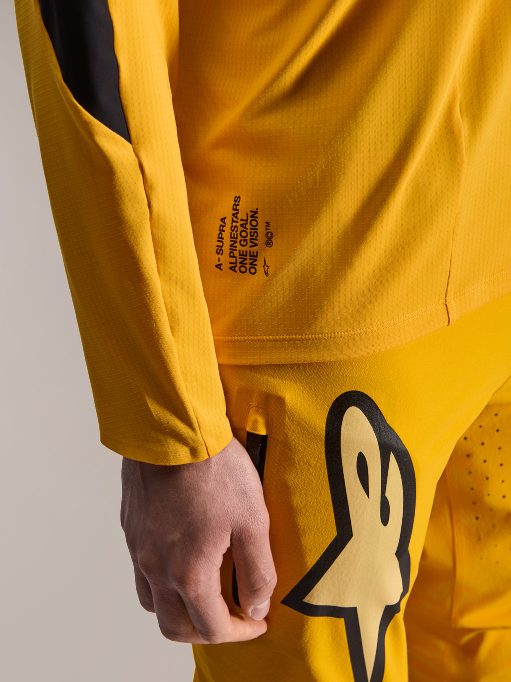 Ensemble d'équipement Alpinestars Limited Edition A-Supra Melt Gold, gros plan du maillot à manches longues jaune foncé et du pantalon assorti, avec le marquage 'One Goal. One Vision.' et un grand logo Astars, tissu technique micro-perforé pour le VTT