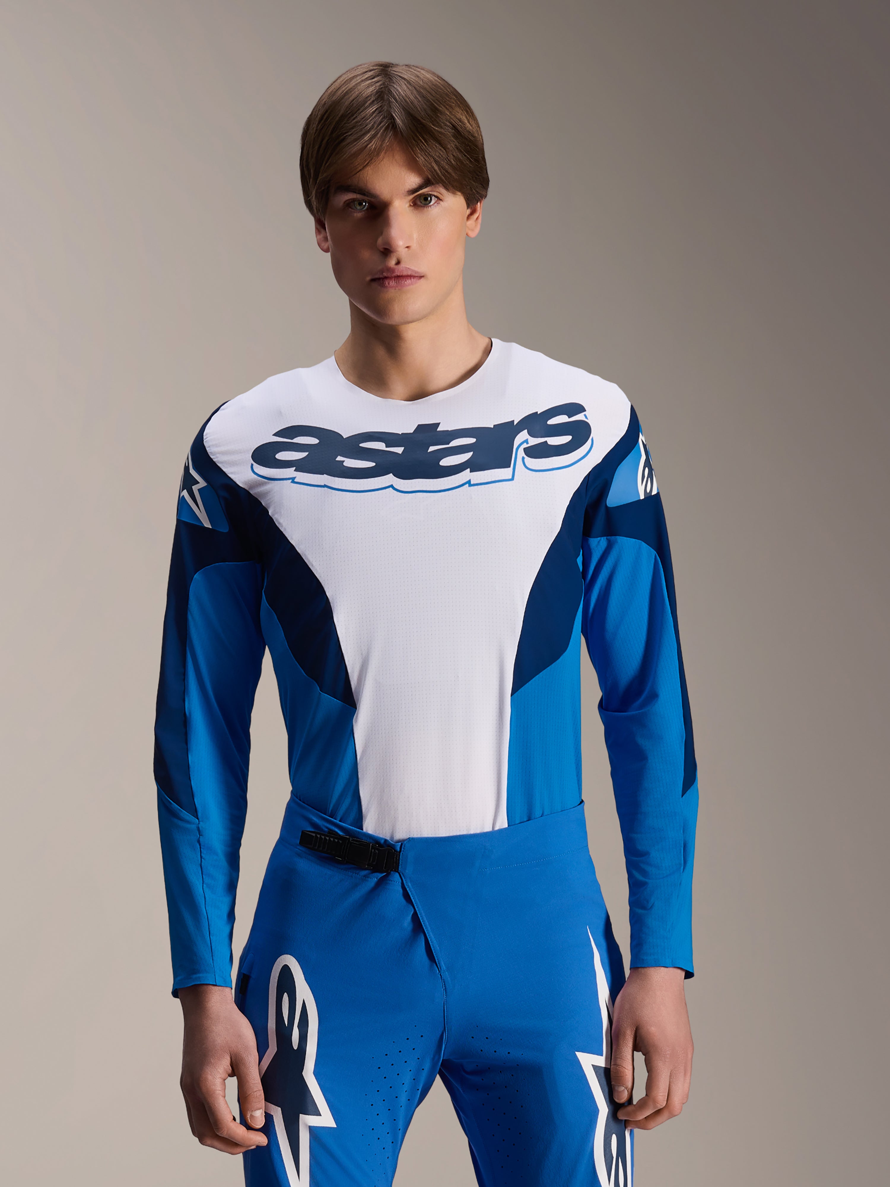 Maillot à manches longues Alpinestars A-Supra Melt, maillot de VTT bleu et blanc, logo astars imposant sur la poitrine, manches bleu foncé, porté avec un pantalon de course bleu assorti avec logos étoiles blancs, équipement de VTT haute performance