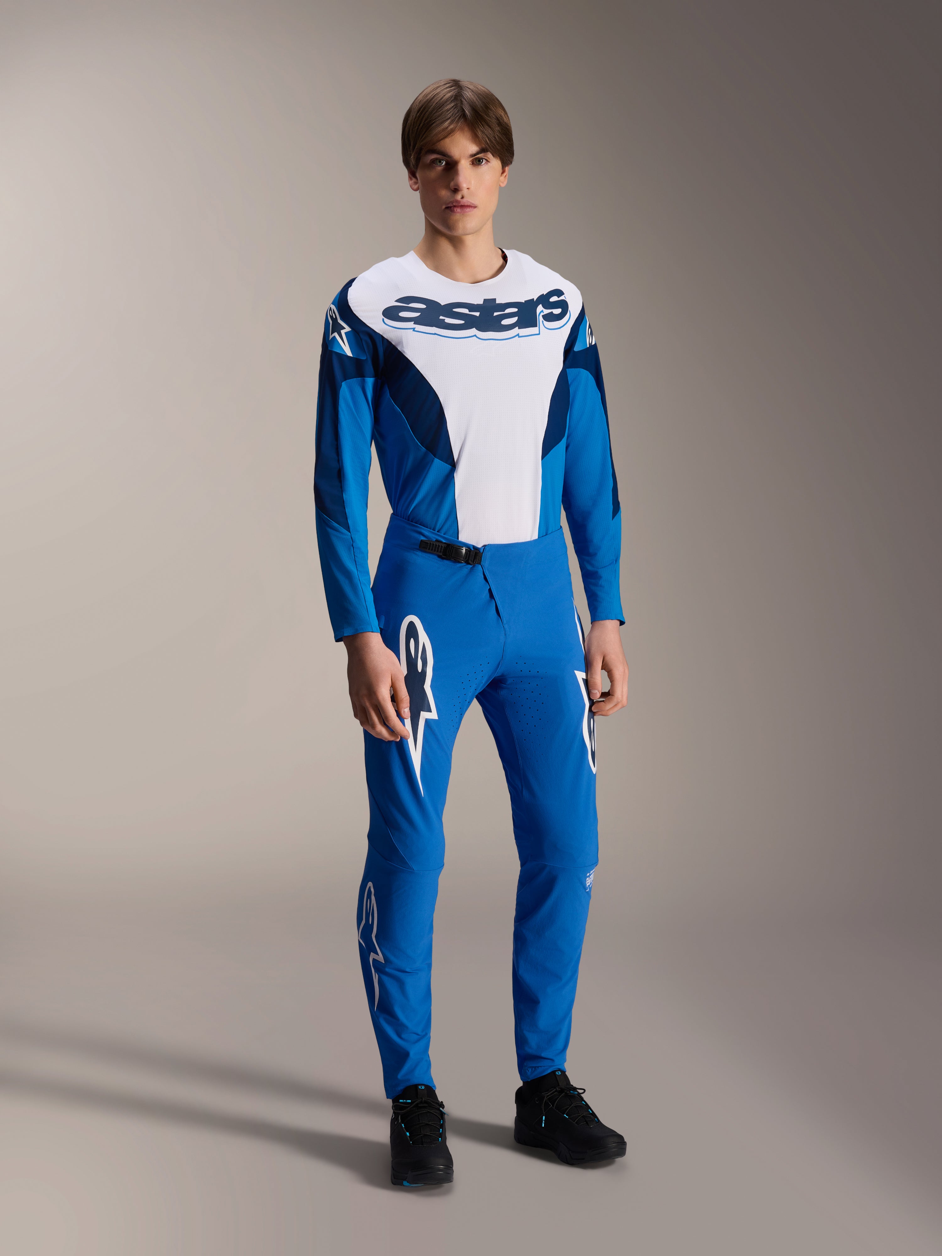 Mannequin portant une tenue de course VTT Alpinestars complète, maillot à manches longues bleu et blanc avec marquage 'astars', pantalon A-Supra Melt bleu assorti avec logos d'étoiles blancs, vêtements de VTT professionnels pour la conduite tout-terrain