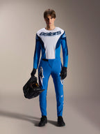 Pilote portant le maillot à manches longues Alpinestars A-Supra Melt bleu et blanc, avec le logo « astars » sur la poitrine, un pantalon bleu assorti, des gants noirs et tenant un casque noir, tenue de course VTT haute performance