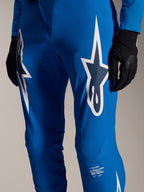 Alpinestars A-Supra Melt Pants, pantalon de cyclisme bleu avec de grands logos Astars blancs sur les cuisses, perforations au laser pour la circulation de l'air et marquage emblématique sur le bas de la jambe, porté avec des gants noirs, équipement de VTT haute performance