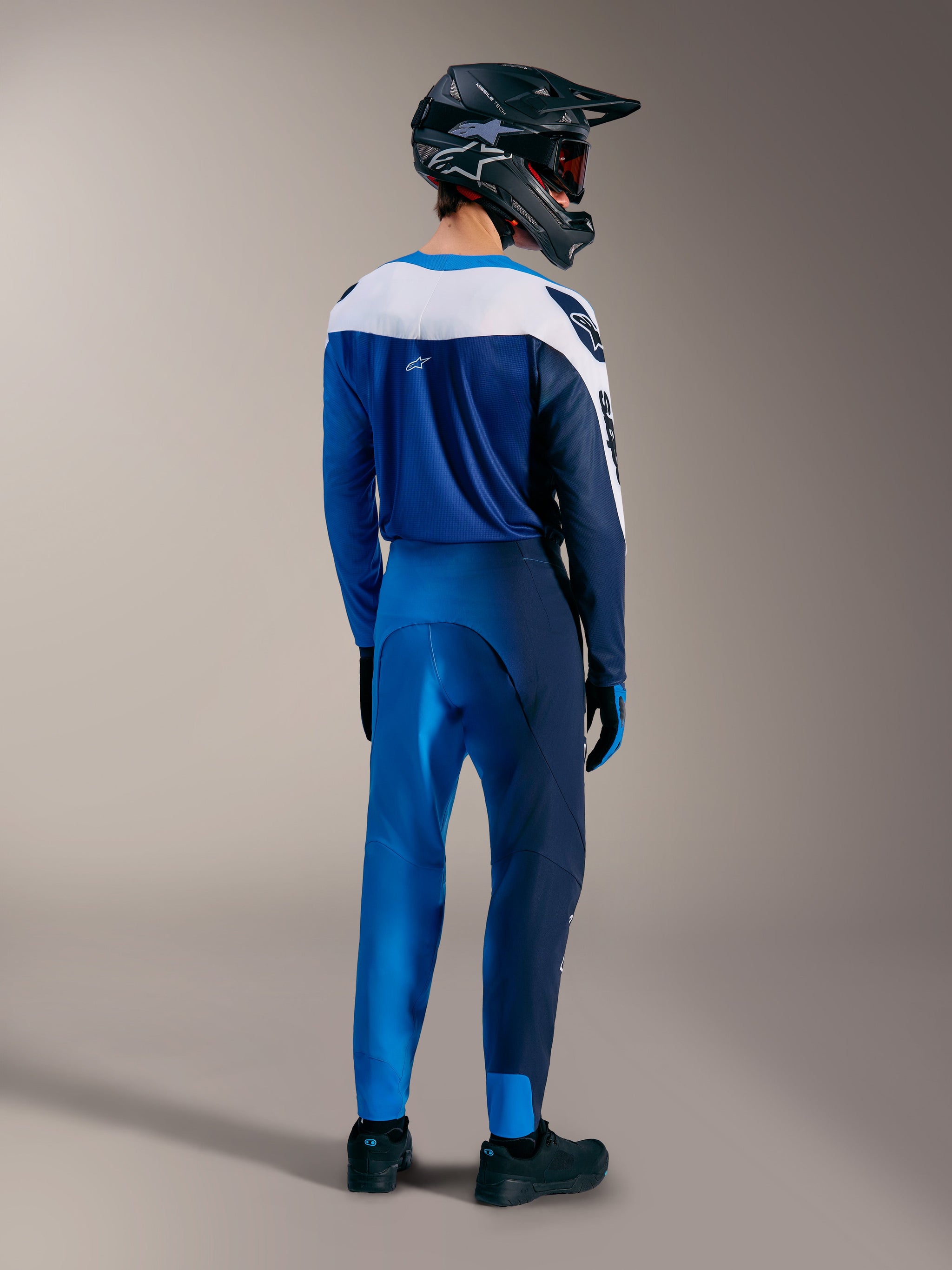 Ensemble VTT A-Supra Elite en Faded Bright Blue, maillot et pantalon Alpinestars vus de dos avec casque intégral.