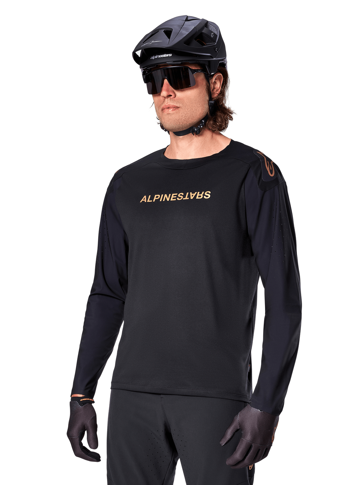 Maillot à manches longues Alpinestars A-Aria Polartec Switch, noir avec logo doré, vêtement de VTT, porté avec un casque noir et des lunettes de soleil, doté de ventilations découpées au laser sur les manches et d'un tissu Polartec évacuant l'humidité pour des performances tout-terrain
