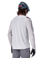Alpinestars A-Aria Polartec Switch Long Sleeve Jersey, Light Gray, seen from the back on a rider, worn with a blue mountain bike helmet and gray pants, performance mountain bike apparel for off-road trails
